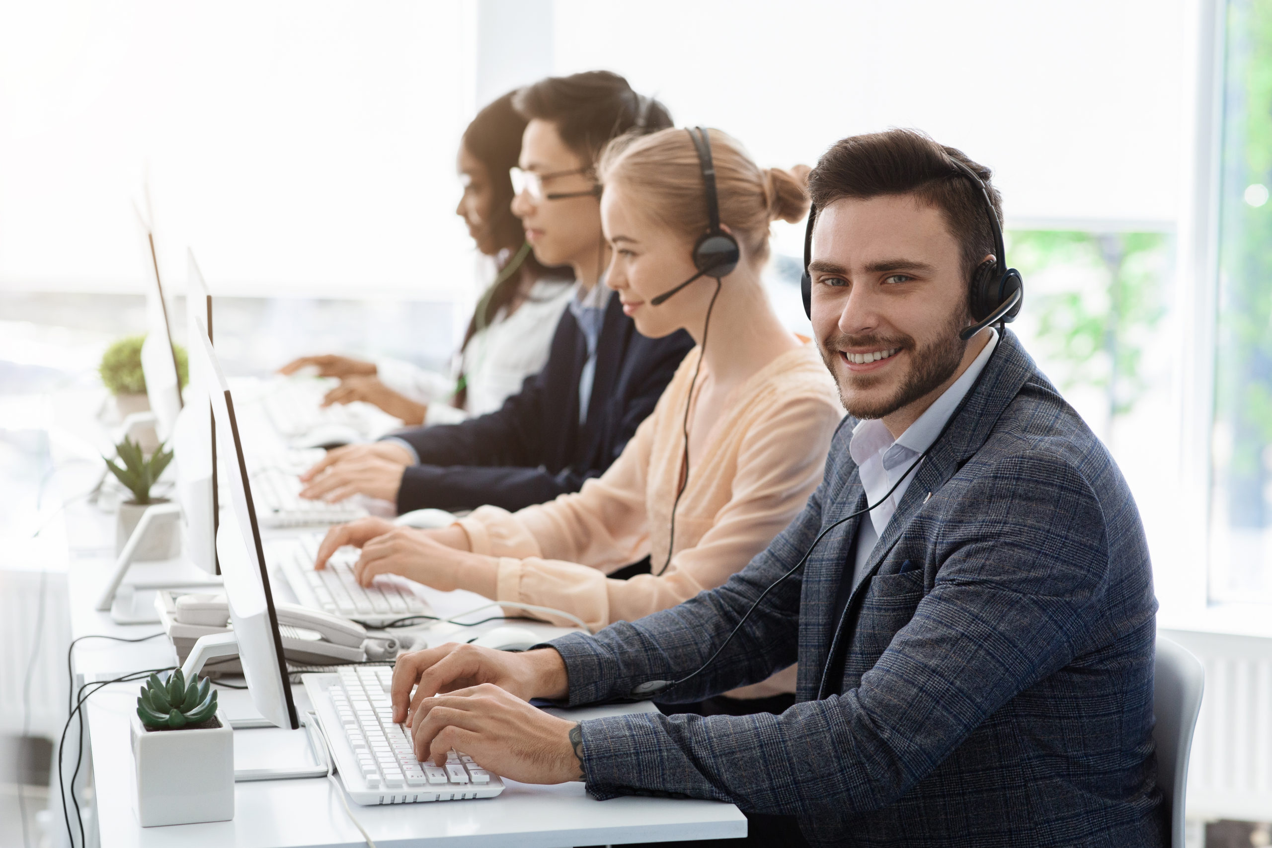Team of customer service agents with headsets working at computers in office, copy space